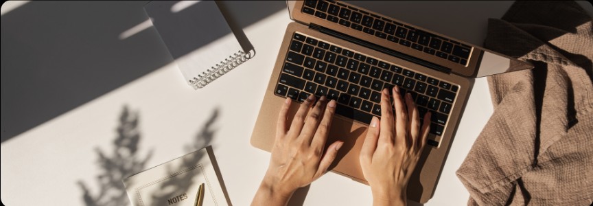 Hands typing on a laptop at a sunlit desk